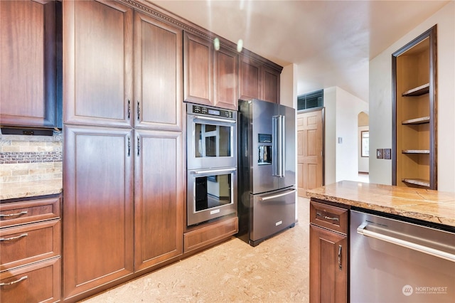212 Grandview Ave, Camano Island, WA 98282 - kitchen with light stone countertops, arched walkways, brown cabinetry, backsplash, and stainless steel appliances
