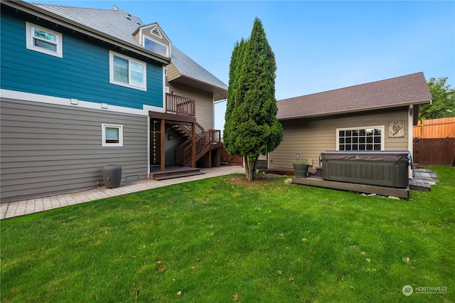 back of property featuring a hot tub, a wooden deck, and a lawn