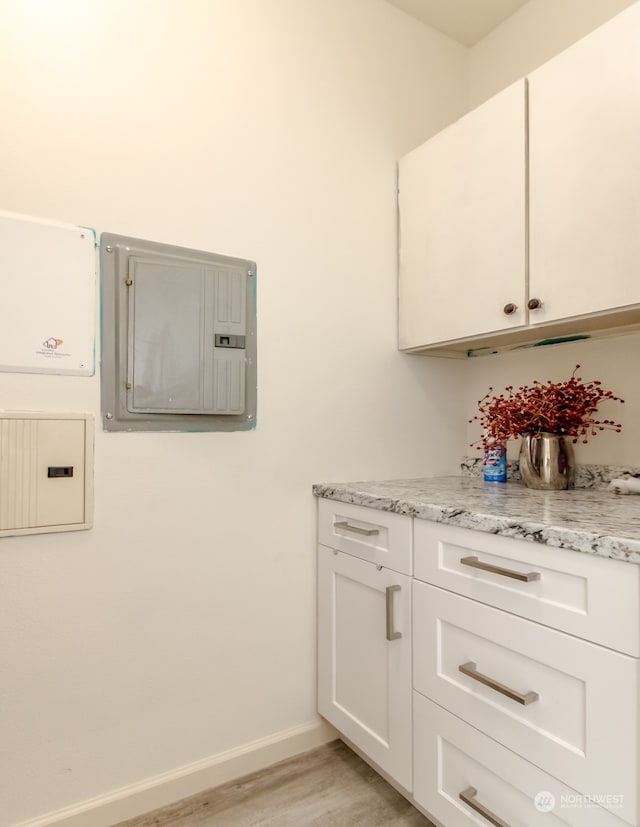 interior space featuring light stone countertops, electric panel, light wood-type flooring, and white cabinets