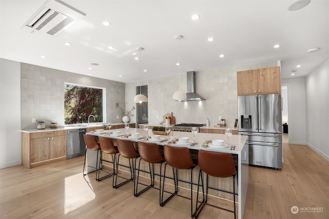 kitchen featuring a large island with sink, a breakfast bar area, wall chimney exhaust hood, stainless steel appliances, and light hardwood / wood-style floors