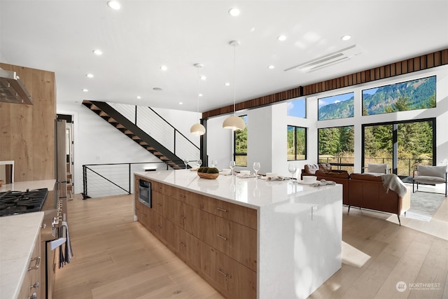 kitchen with stainless steel gas cooktop, light hardwood / wood-style flooring, a large island, ventilation hood, and pendant lighting