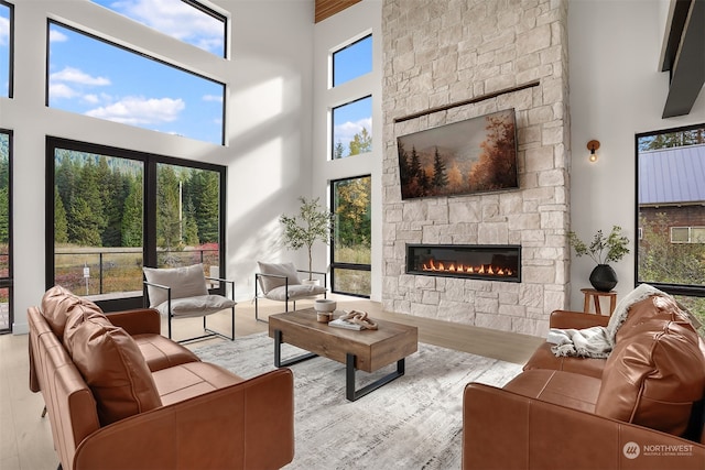 living room featuring light hardwood / wood-style flooring, a stone fireplace, and a high ceiling