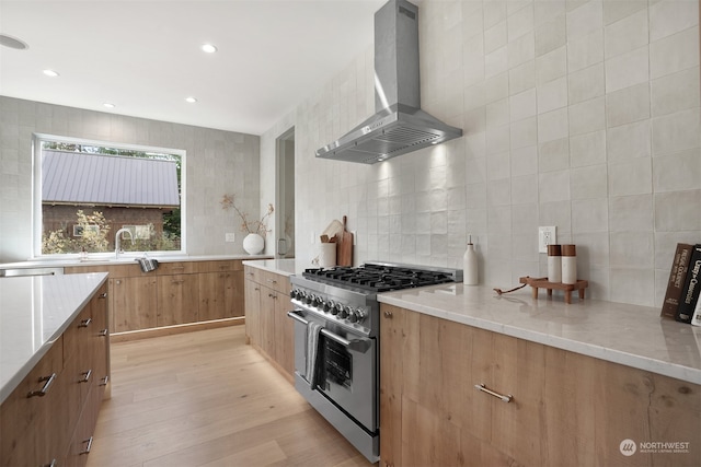 kitchen featuring wall chimney range hood, light stone countertops, light wood-type flooring, sink, and high end range