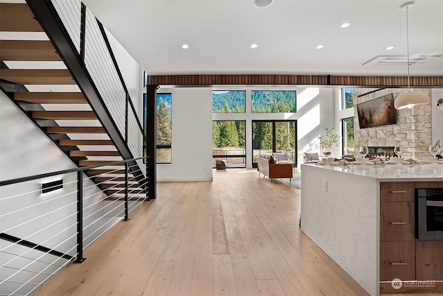 kitchen with a stone fireplace, stainless steel oven, decorative light fixtures, light stone counters, and light hardwood / wood-style flooring