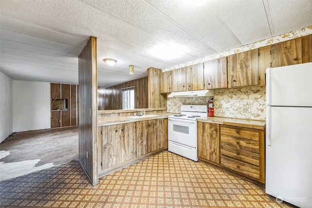 kitchen with sink, wooden walls, a textured ceiling, and white appliances