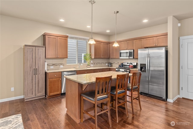 kitchen with sink, a kitchen island, stainless steel appliances, dark wood-type flooring, and light stone counters