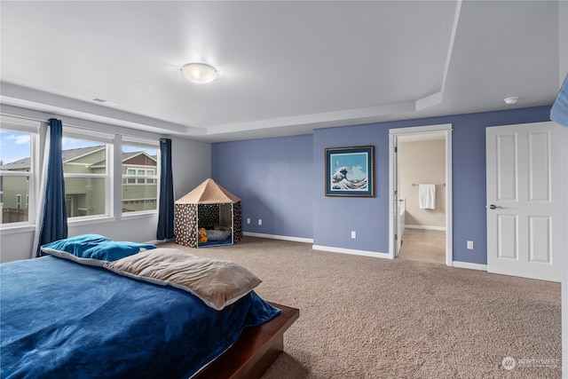 carpeted bedroom featuring ensuite bathroom and a raised ceiling