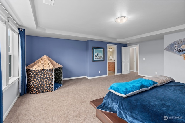 bedroom featuring ensuite bathroom, carpet flooring, and a raised ceiling