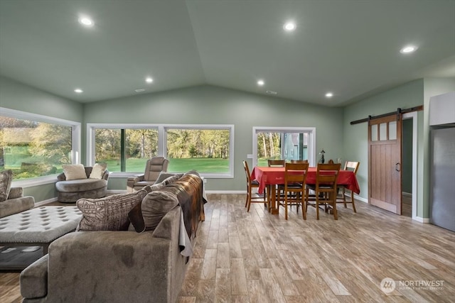 living room with a barn door, light wood-type flooring, and vaulted ceiling