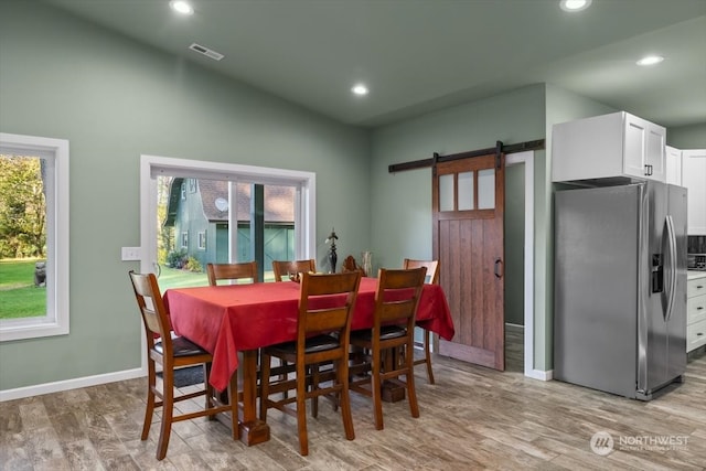 dining space with lofted ceiling, a barn door, plenty of natural light, and light wood-type flooring