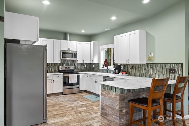 kitchen featuring kitchen peninsula, stainless steel appliances, sink, light wood-type flooring, and white cabinets