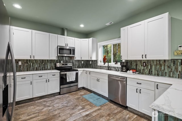 kitchen with dark wood-type flooring, sink, light stone countertops, white cabinetry, and appliances with stainless steel finishes