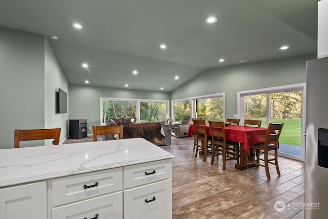 kitchen featuring vaulted ceiling, stainless steel fridge with ice dispenser, light wood-type flooring, white cabinetry, and light stone counters