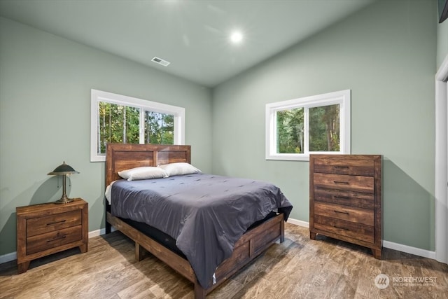 bedroom featuring vaulted ceiling, hardwood / wood-style flooring, and multiple windows