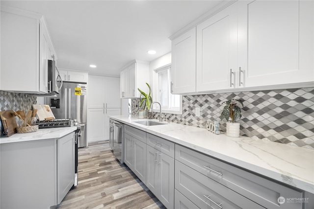 kitchen with sink, appliances with stainless steel finishes, light hardwood / wood-style flooring, and tasteful backsplash