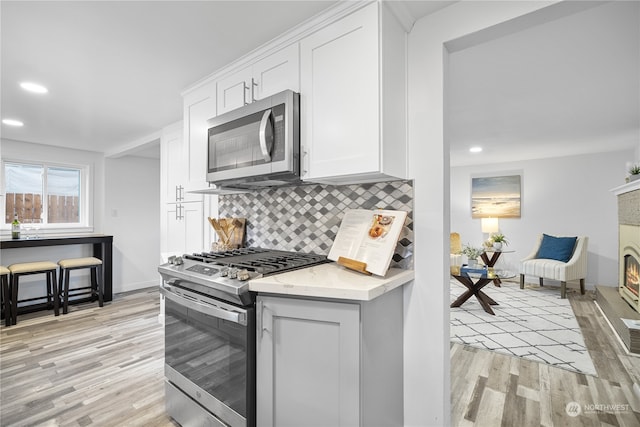 kitchen with light wood-type flooring, backsplash, stainless steel appliances, white cabinets, and light stone counters