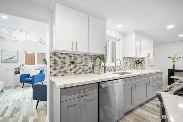 kitchen with sink, dishwasher, light hardwood / wood-style floors, light stone counters, and decorative backsplash