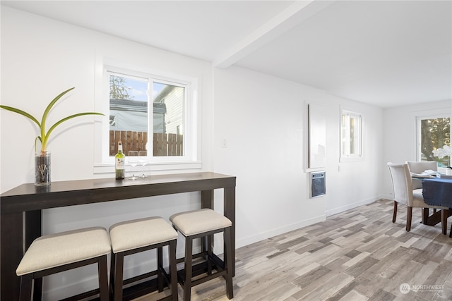 dining space featuring light hardwood / wood-style flooring, beamed ceiling, heating unit, and a wealth of natural light