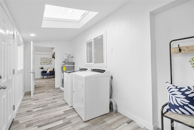 laundry area with light hardwood / wood-style flooring, a skylight, washer and clothes dryer, and strapped water heater