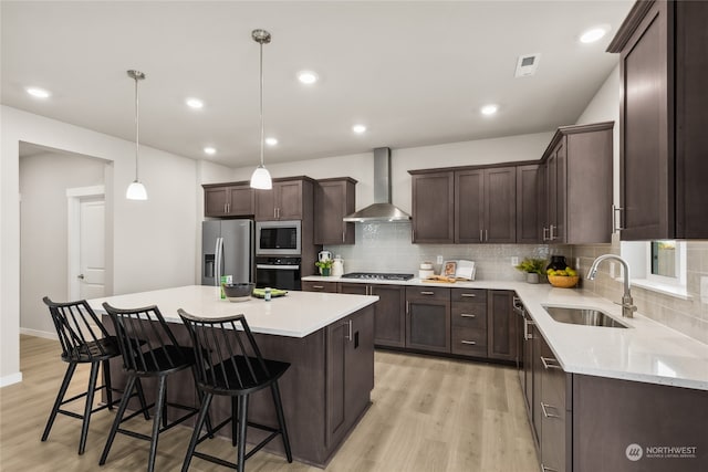 kitchen with a center island, appliances with stainless steel finishes, sink, and wall chimney range hood