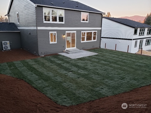 back house at dusk with ac unit, a lawn, and a patio area