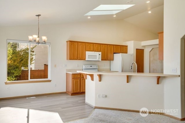 kitchen featuring a breakfast bar area, kitchen peninsula, pendant lighting, a chandelier, and white appliances