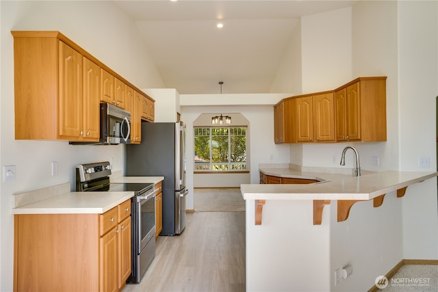 kitchen featuring baseboards, light countertops, a kitchen bar, appliances with stainless steel finishes, and a peninsula