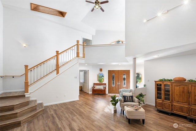 living room featuring hardwood / wood-style floors, ceiling fan, high vaulted ceiling, and a skylight