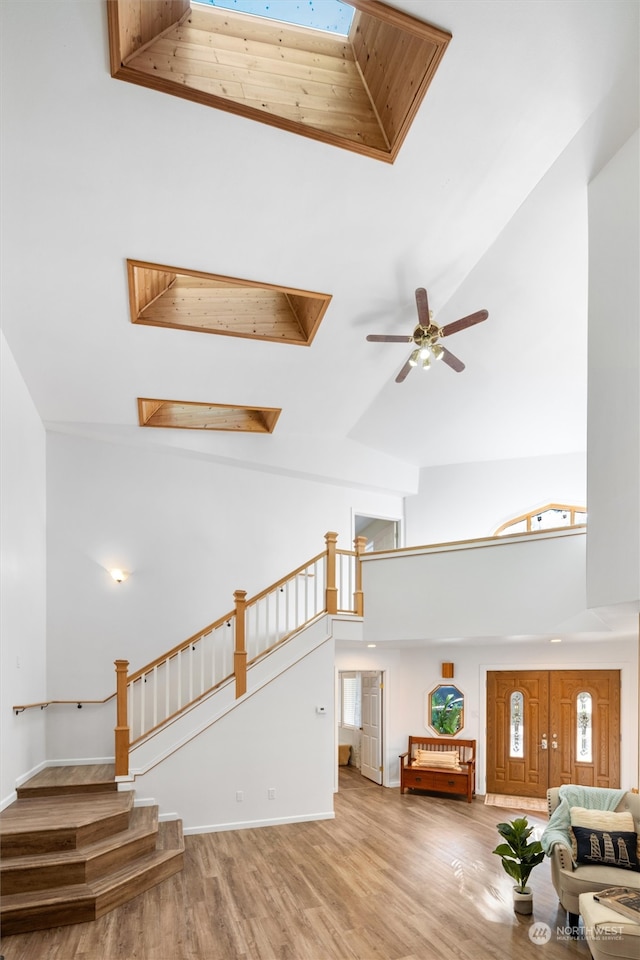 unfurnished living room with hardwood / wood-style flooring, high vaulted ceiling, a skylight, and ceiling fan