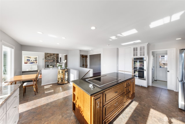 kitchen featuring cooktop, a fireplace, a center island, double oven, and white cabinets