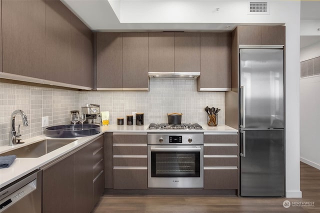 kitchen with sink, dark wood-type flooring, appliances with stainless steel finishes, and tasteful backsplash