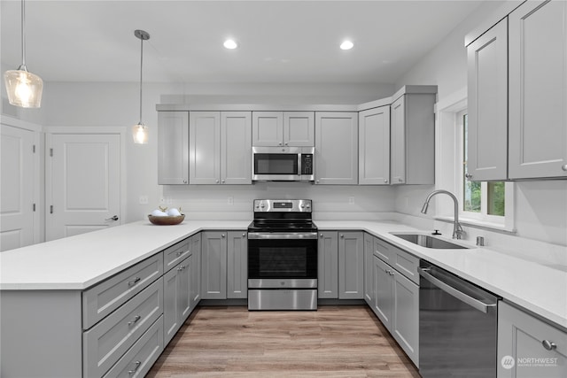 kitchen with sink, decorative light fixtures, light wood-type flooring, gray cabinets, and appliances with stainless steel finishes