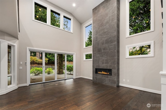 unfurnished living room with high vaulted ceiling, a tile fireplace, and dark hardwood / wood-style flooring