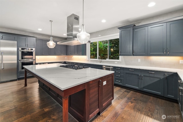 kitchen featuring appliances with stainless steel finishes, island range hood, hanging light fixtures, light stone counters, and dark hardwood / wood-style floors