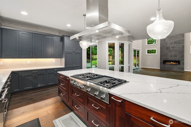 kitchen with stainless steel gas cooktop, hanging light fixtures, island range hood, and dark hardwood / wood-style flooring