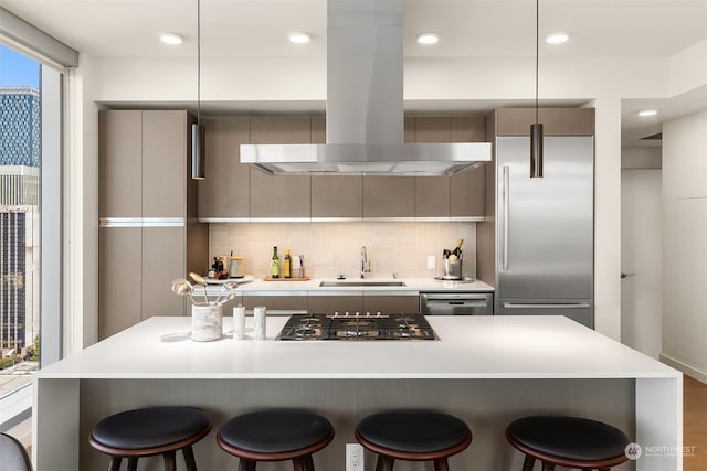 kitchen with appliances with stainless steel finishes, sink, island exhaust hood, a kitchen breakfast bar, and hanging light fixtures