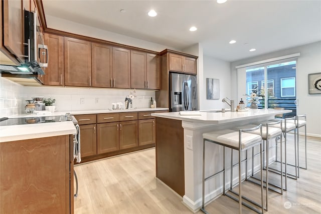 kitchen featuring backsplash, a breakfast bar area, stainless steel appliances, light hardwood / wood-style flooring, and a kitchen island with sink