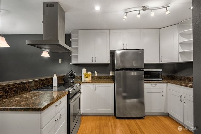 kitchen with appliances with stainless steel finishes, wall chimney exhaust hood, white cabinets, and light hardwood / wood-style floors