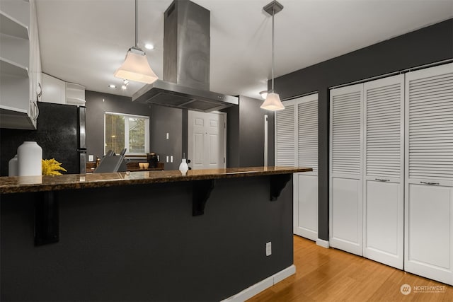 kitchen with island range hood, pendant lighting, white cabinets, light hardwood / wood-style floors, and stainless steel refrigerator