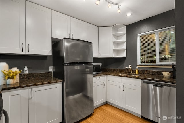 kitchen featuring appliances with stainless steel finishes, sink, light hardwood / wood-style floors, dark stone counters, and white cabinets