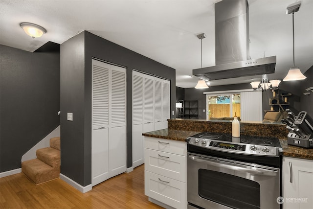 kitchen with white cabinetry, island range hood, stainless steel electric range oven, dark stone counters, and decorative light fixtures