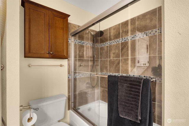 bathroom featuring toilet and shower / bath combination with glass door