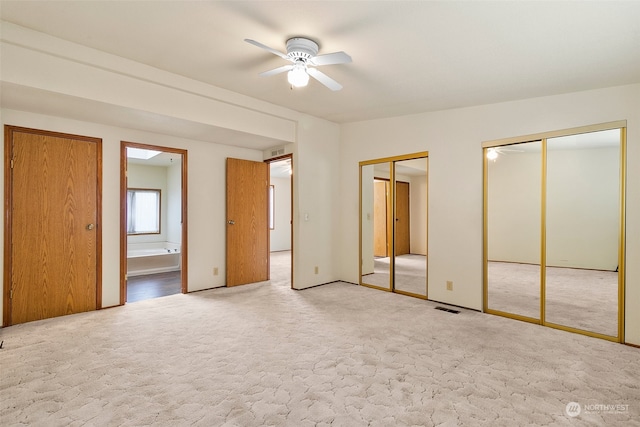 unfurnished bedroom featuring ceiling fan, light carpet, connected bathroom, and multiple closets