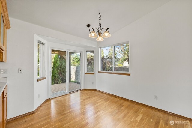 unfurnished dining area featuring lofted ceiling, an inviting chandelier, and light wood-type flooring