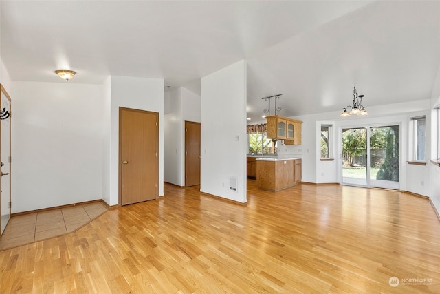 unfurnished living room featuring light hardwood / wood-style floors, lofted ceiling, and a chandelier