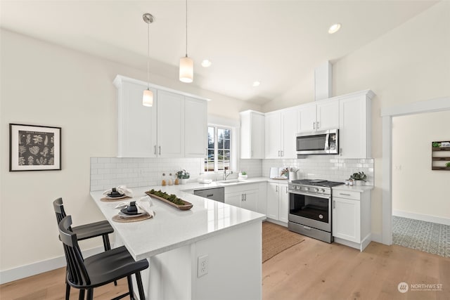 kitchen featuring appliances with stainless steel finishes, light hardwood / wood-style flooring, white cabinetry, and hanging light fixtures