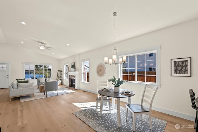 dining room with ceiling fan with notable chandelier, lofted ceiling, light wood-type flooring, and a fireplace