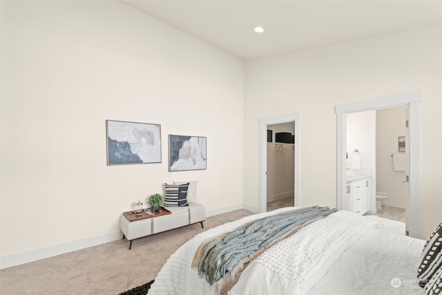 bedroom featuring a spacious closet, connected bathroom, light colored carpet, and a closet