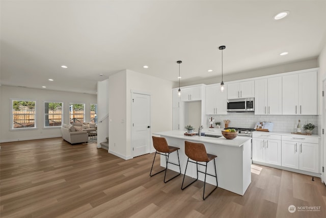 kitchen with light wood-type flooring, an island with sink, hanging light fixtures, a kitchen breakfast bar, and white cabinets