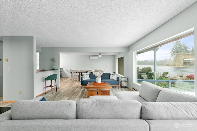 living room with an AC wall unit, a textured ceiling, a water view, light hardwood / wood-style floors, and ceiling fan